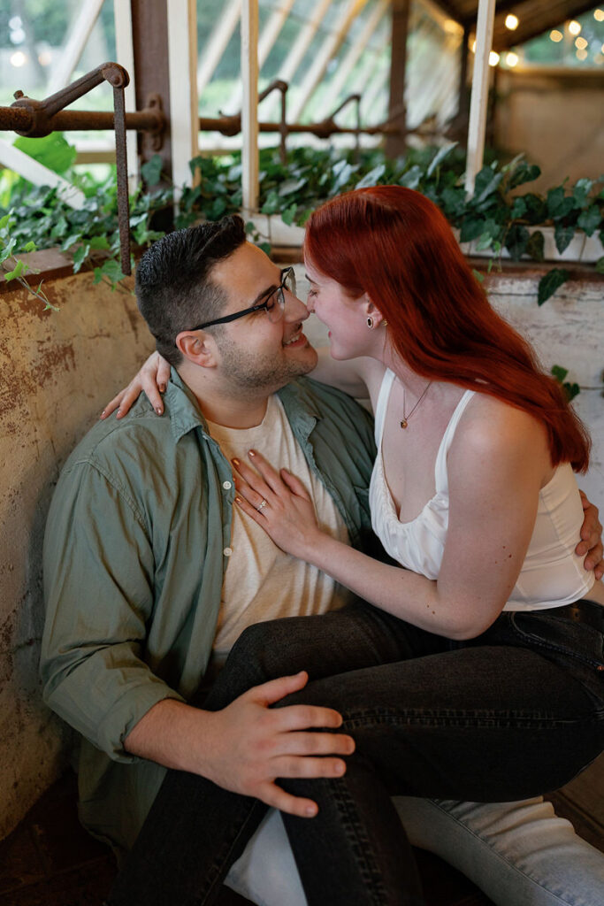 A person sitting on their partner's lap as they are both smiling closely at each other 