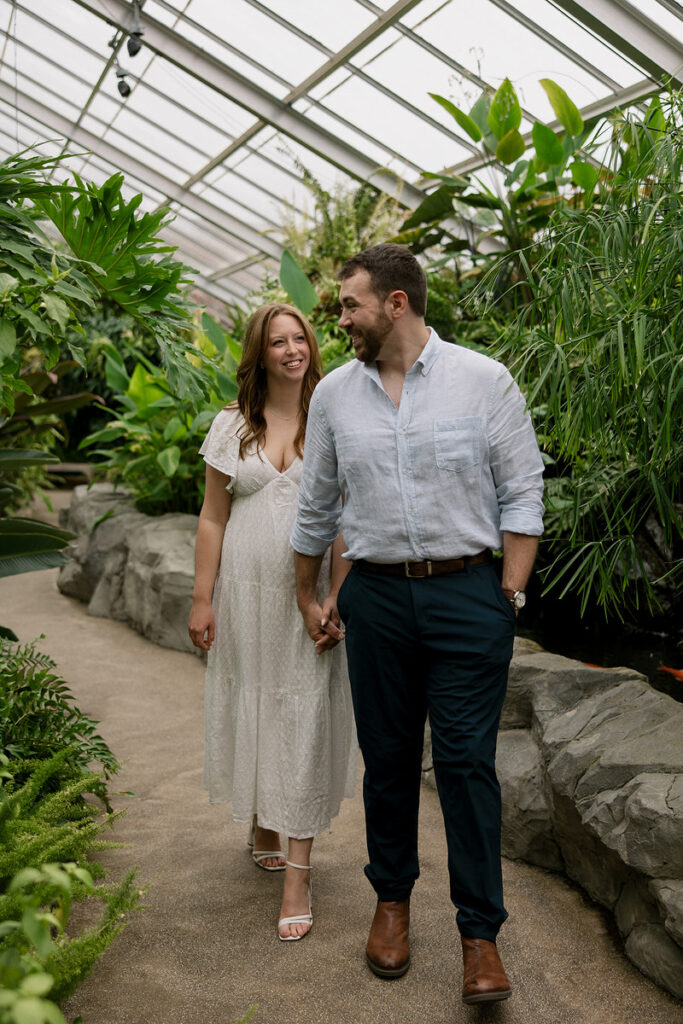 A couple holding hands and walking through a greenhouse 