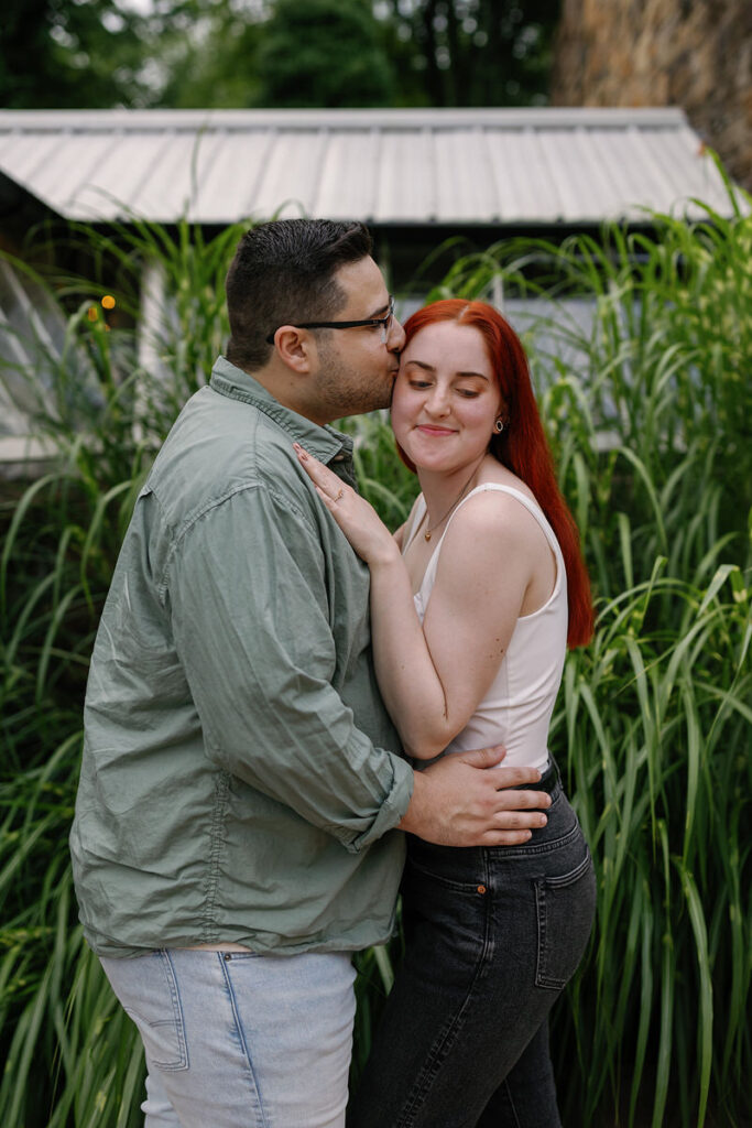 A person kissing their partner's head as they stand in a garden 
